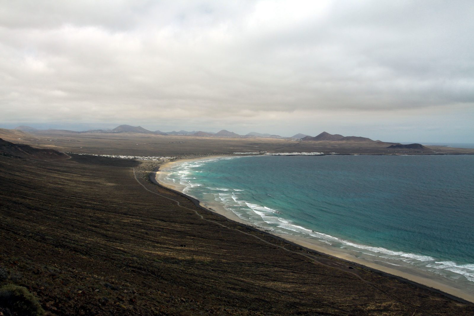 Brede baai met turquoise water en lange zandstrook bij Famara op Lanzarote